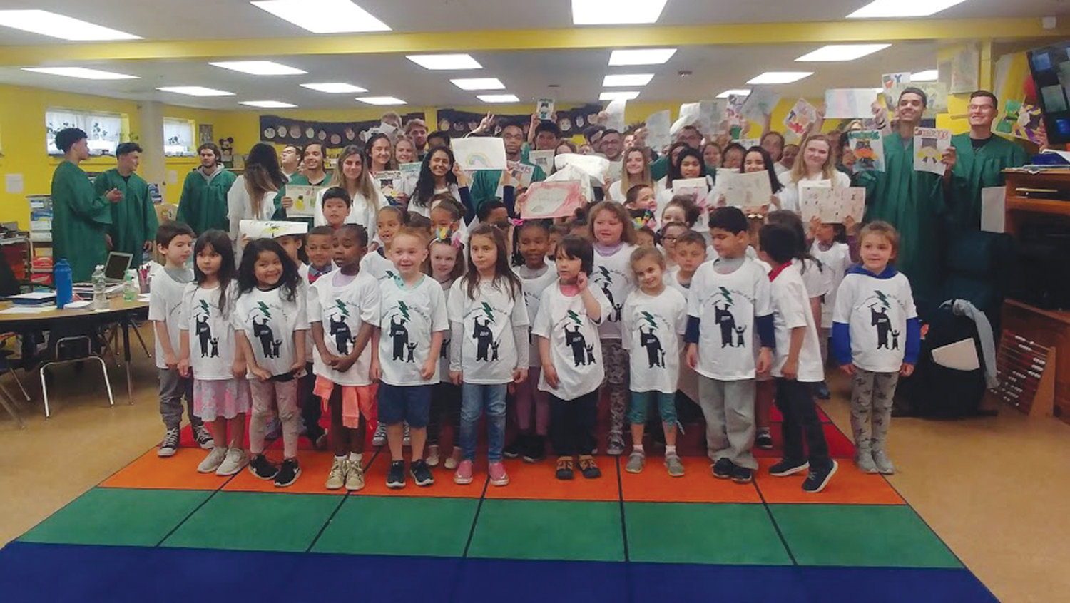 GIFTS FOR THE GRADS: The kindergarten students from Edgewood Highland Elementary School pose with the East graduates, with the kindergarteners wearing special T-shirts and the seniors holding special cards and posters.